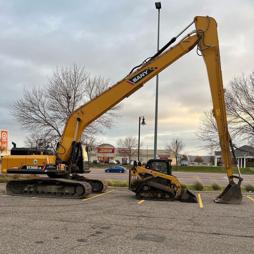 Excavator and compact track loader parked in a lot, showcasing heavy construction equipment.