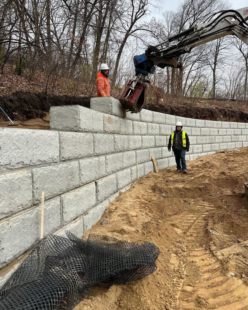 Workers installing a stone retaining wall with machinery on a construction site.